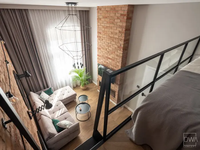 Widok z antresoli sypialnianej na salon z cegłą i żyrandolem geometrycznym - apartament w Krakowie 22m2