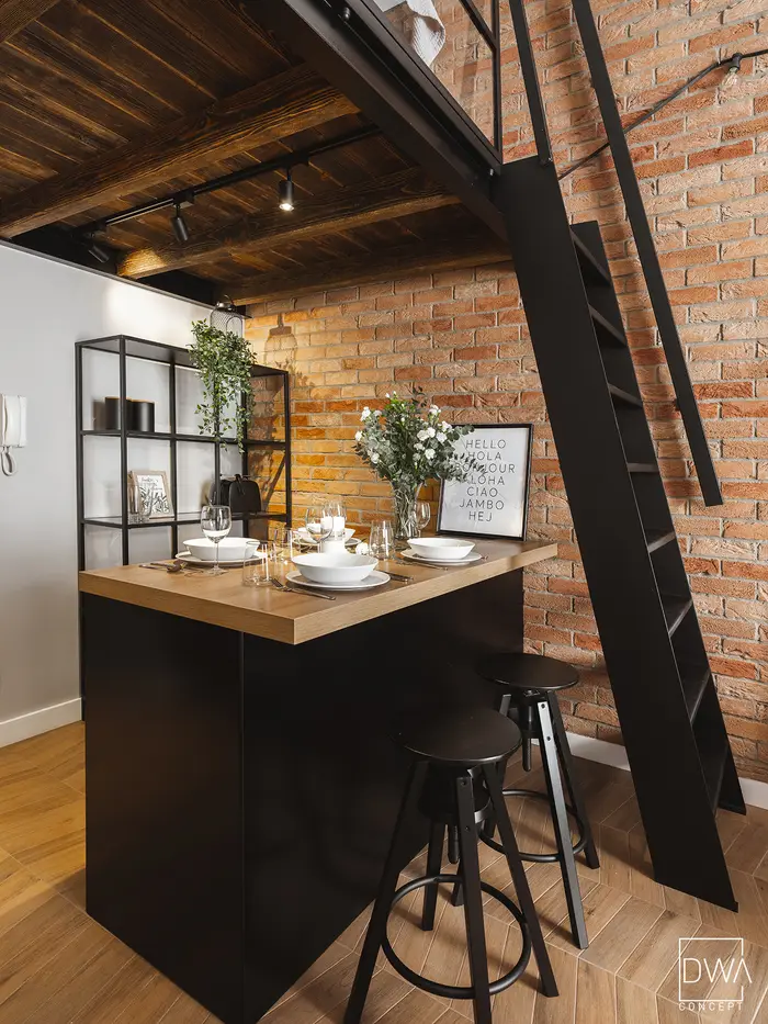 Barek z regałem na rośliny i czarną drabinką prowadzącą na antresolę - apartament w Krakowie 22m2