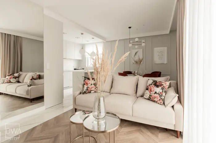 Salon z beżową sofą, kwiecistymi poduszkami i widokiem na kuchnię - apartament 46m2 w Krakowie