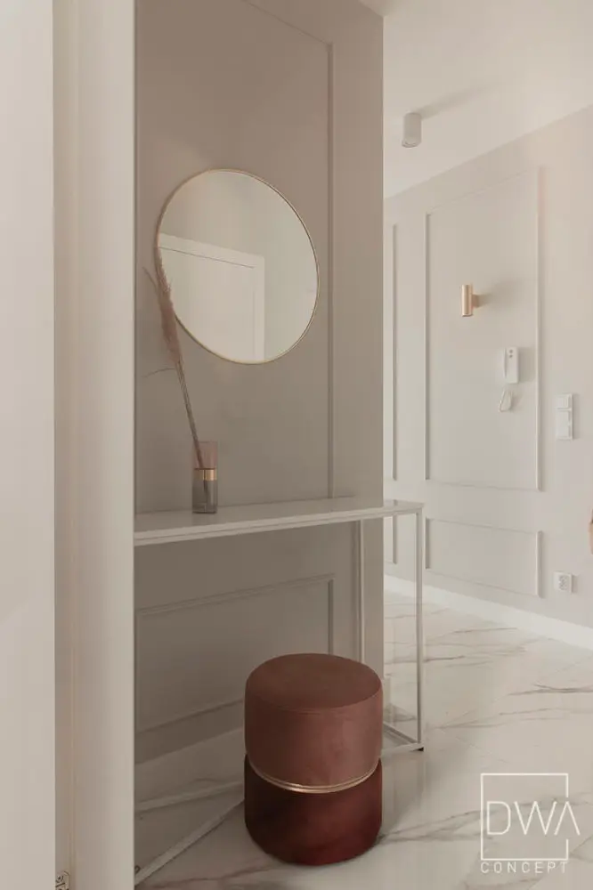 Wnęka z okrągłym lustrem w złotej ramie i bordową pufą - apartament 46m2 w Krakowie